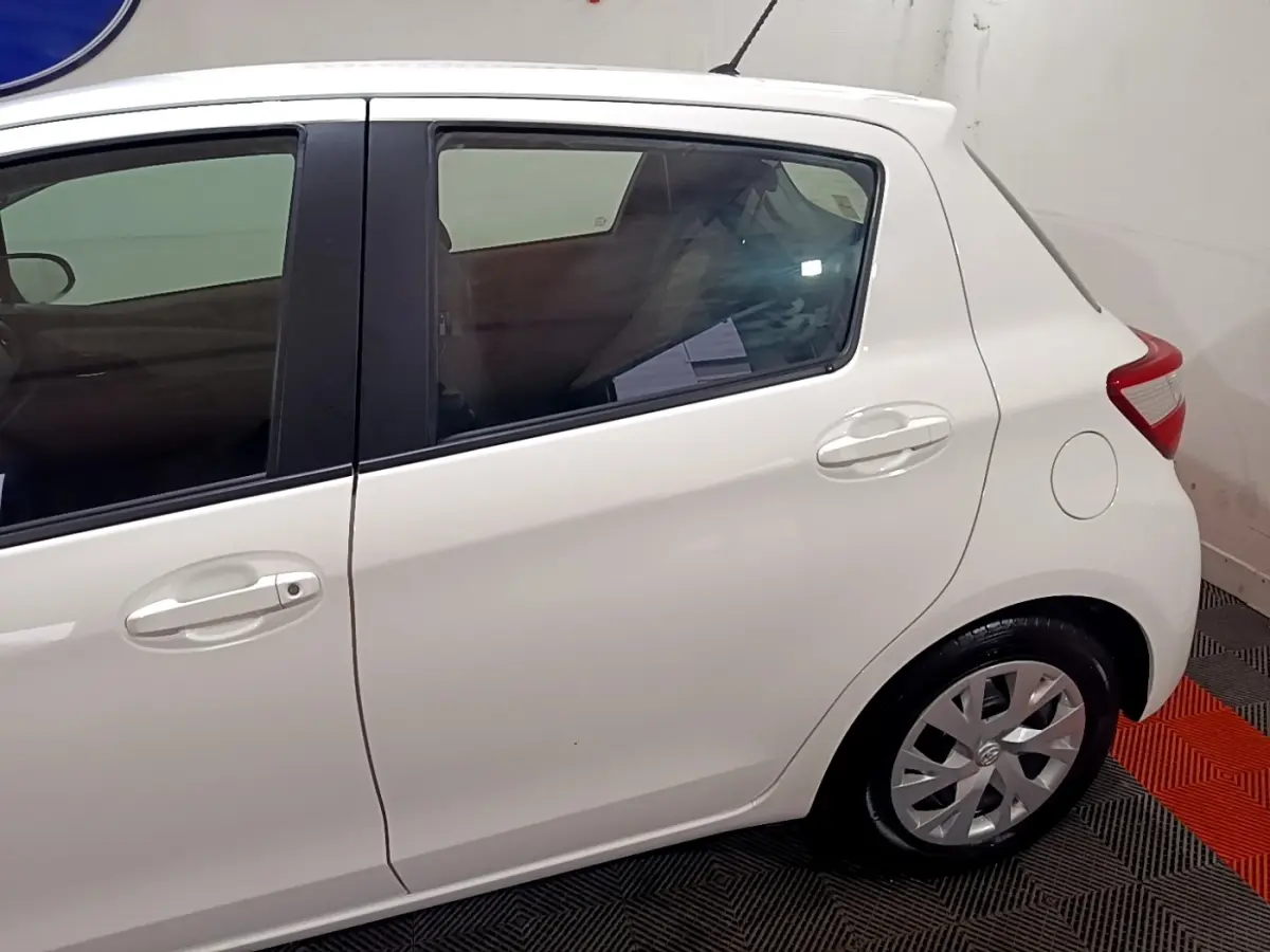 Vue latérale droite d'une Toyota Yaris blanche 2019, mettant en valeur les poignées de porte et la roue arrière.