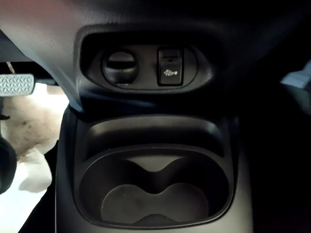 Gros plan sur le porte-gobelets central et commande d'ouverture du capot dans l'habitacle d'une Toyota Yaris blanche.