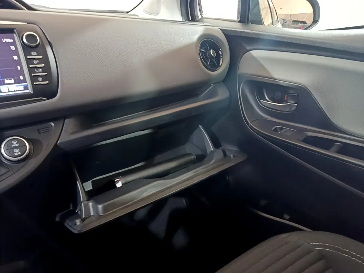 Intérieur côté passager d'une Toyota Yaris blanche 2019, boîte à gants ouverte et tableau de bord avec écran tactile visible.