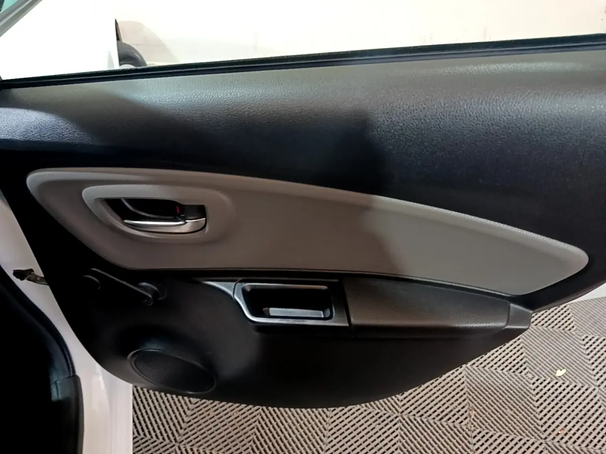 Vue intérieure du panneau de porte côté gauche de la Toyota Yaris blanche, avec poignée argentée et haut-parleur intégré.