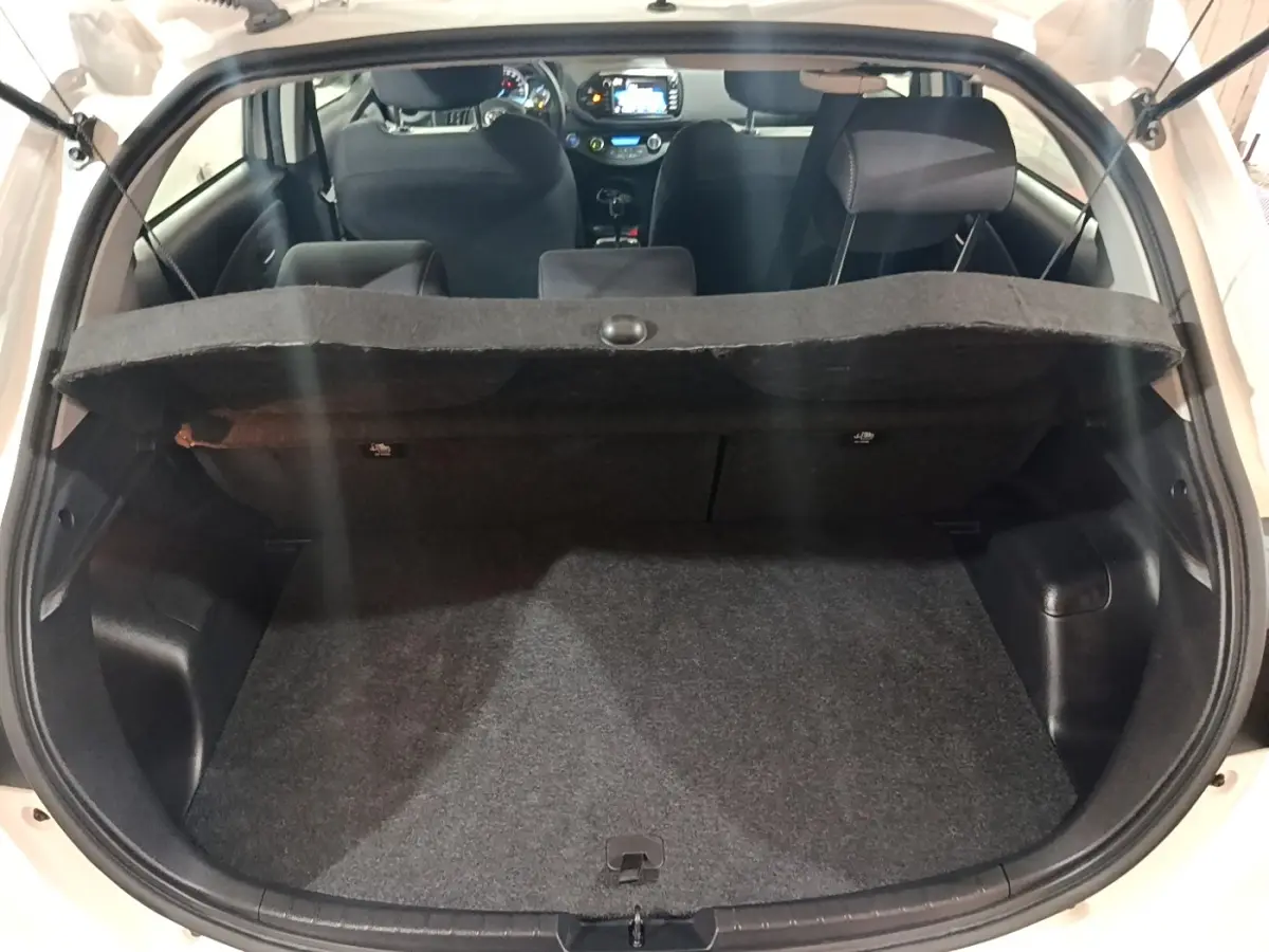 Coffre ouvert d’une Toyota Yaris blanche vue de l’arrière, montrant l’habitacle et la tablette de coffre relevée.