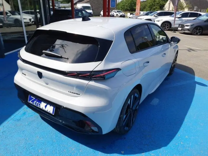 Vue 3/4 arrière droite d'une Peugeot 308 blanche Okénite avec vitres arrière surteintées et jantes alliage noires.