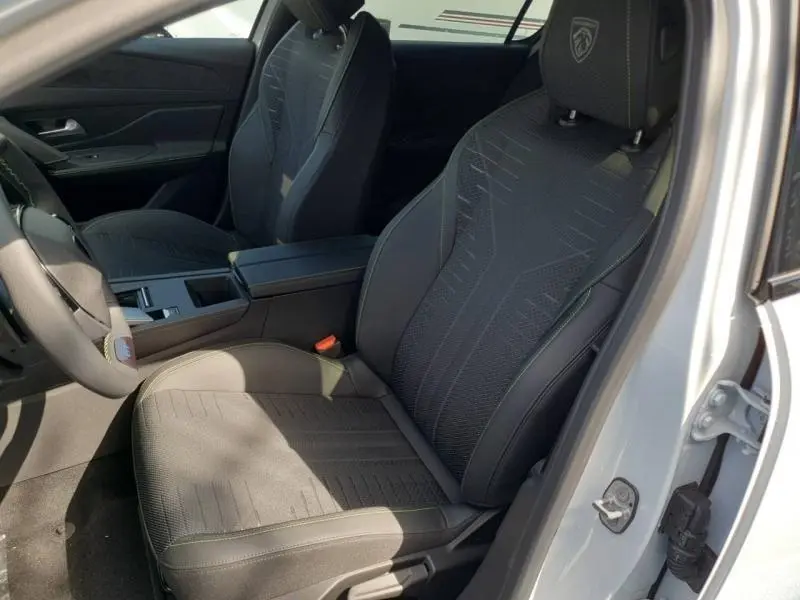 Vue intérieure côté conducteur de la Peugeot 308 Hybrid blanche, sièges noirs avec logo Peugeot brodé sur l'appui-tête.
