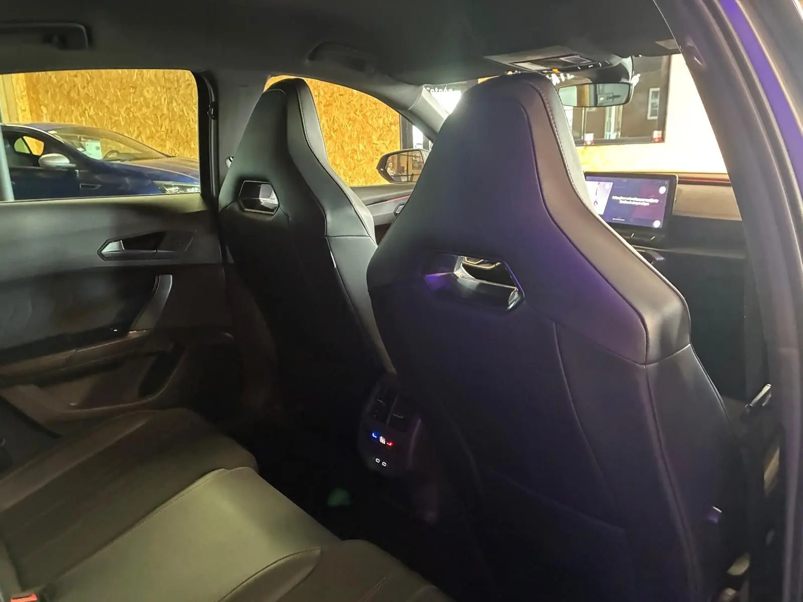 Vue intérieure arrière droite du CUPRA Formentor 1.4 E-HYBRID 2024 avec sièges sport noirs et écran tactile avant visible.
