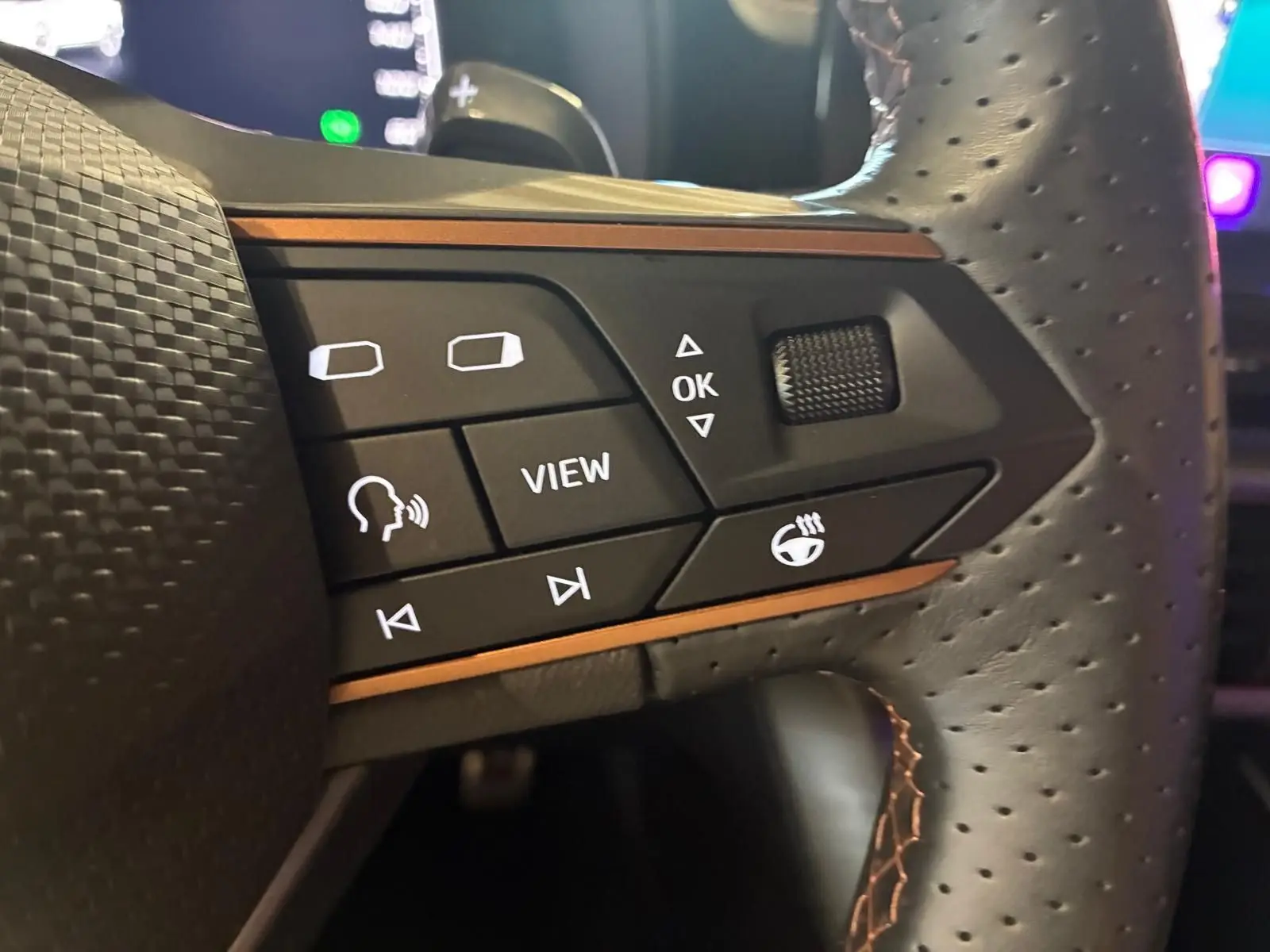 Gros plan sur les commandes du volant perforé du CUPRA Formentor 1.4 E-HYBRID 2024, avec surpiqûres orange et boutons multifonctions.