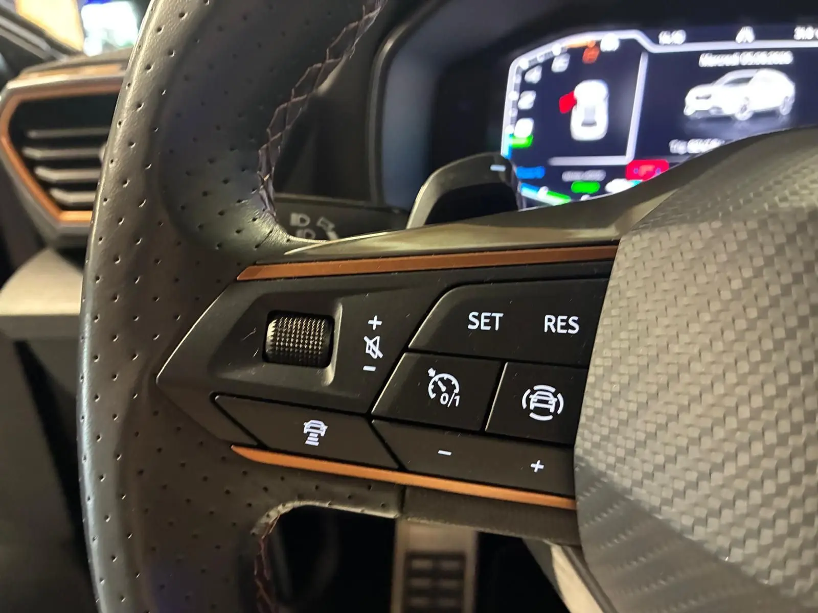 Gros plan sur les commandes gauche du volant perforé noir du CUPRA Formentor gris foncé mat, avec affichage numérique en arrière-plan.