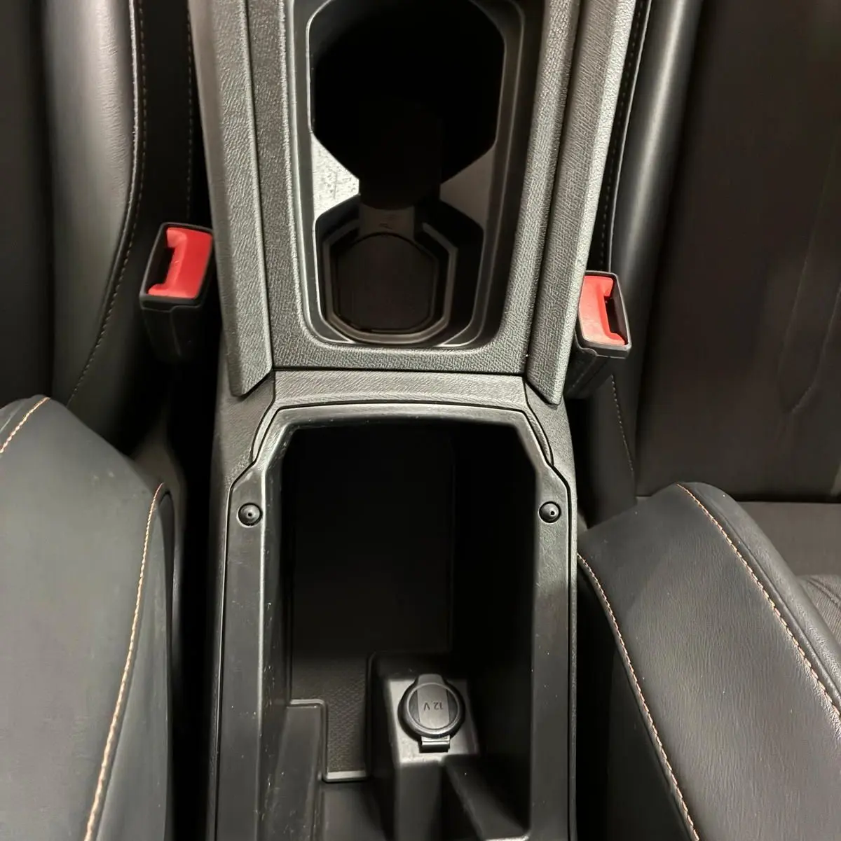 Vue plongeante sur la console centrale noire du CUPRA Formentor 1.4 E-HYBRID avec porte-gobelets et prise 12V visible.