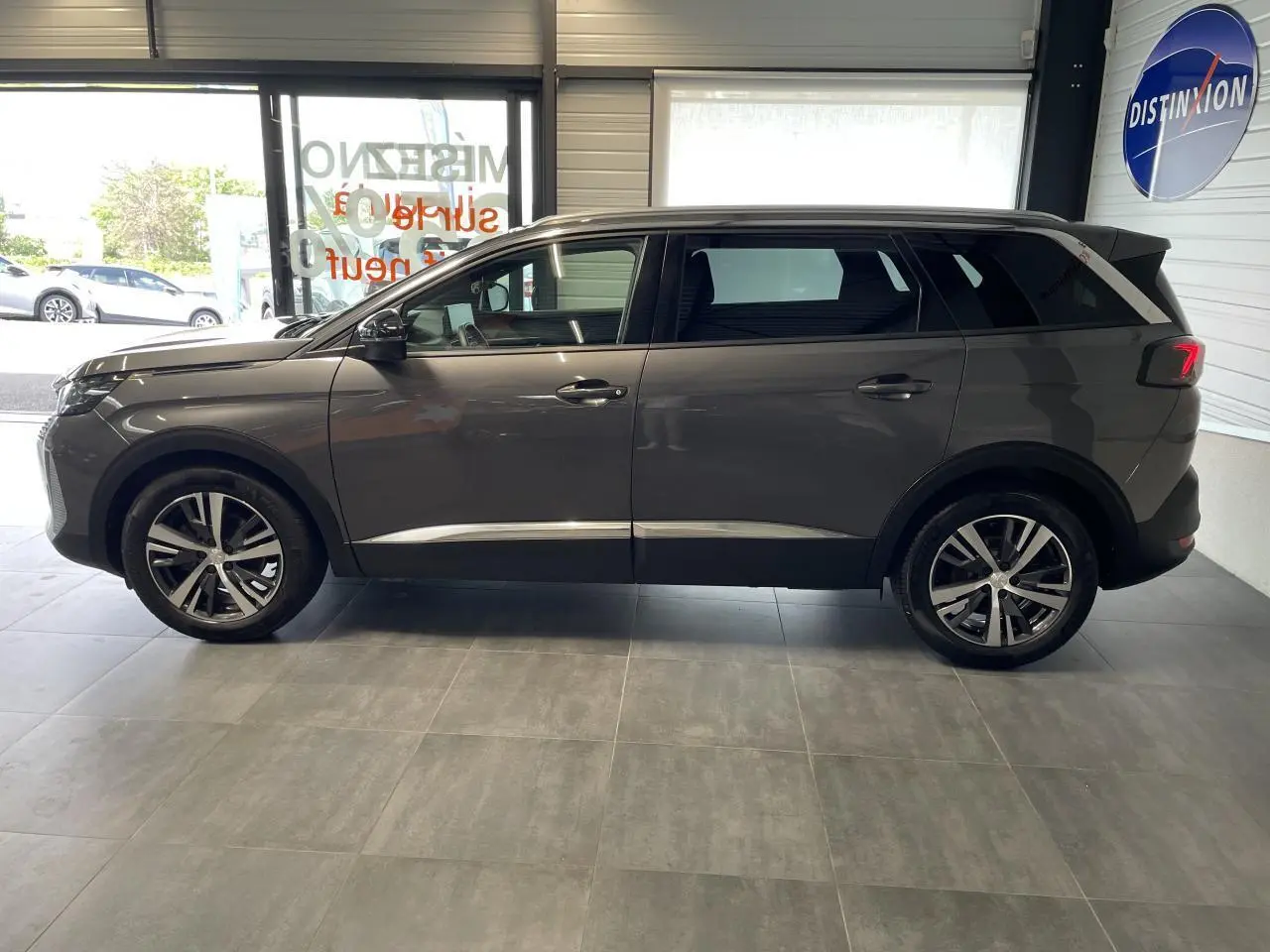 Profil droit du Peugeot 5008 gris platinium 2024 en showroom, avec jantes alliage bi-ton et vitres surteintées.