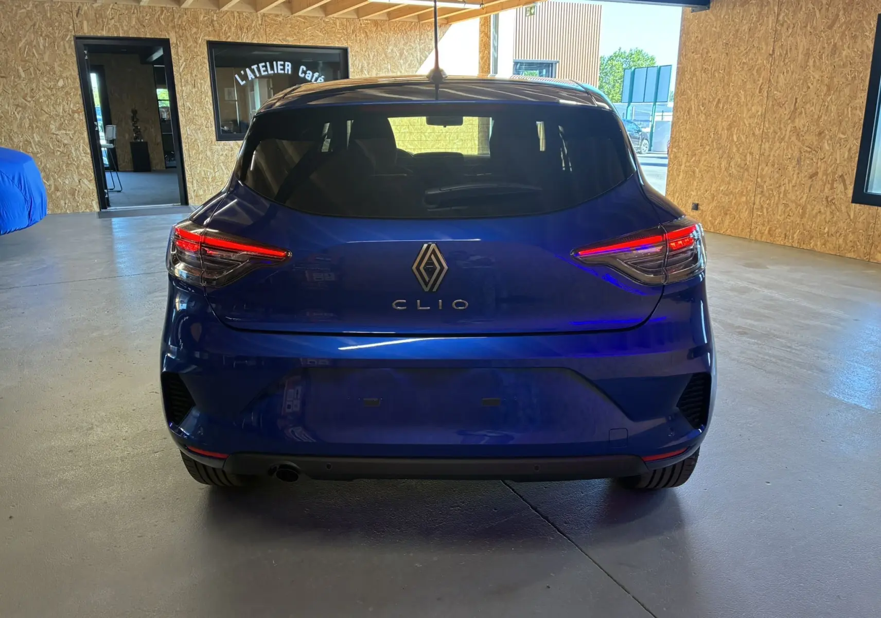 Vue arrière d'une Renault Clio TCE 90CH X-TRONIC Evolution bleu iron, avec feux arrière allumés en intérieur.