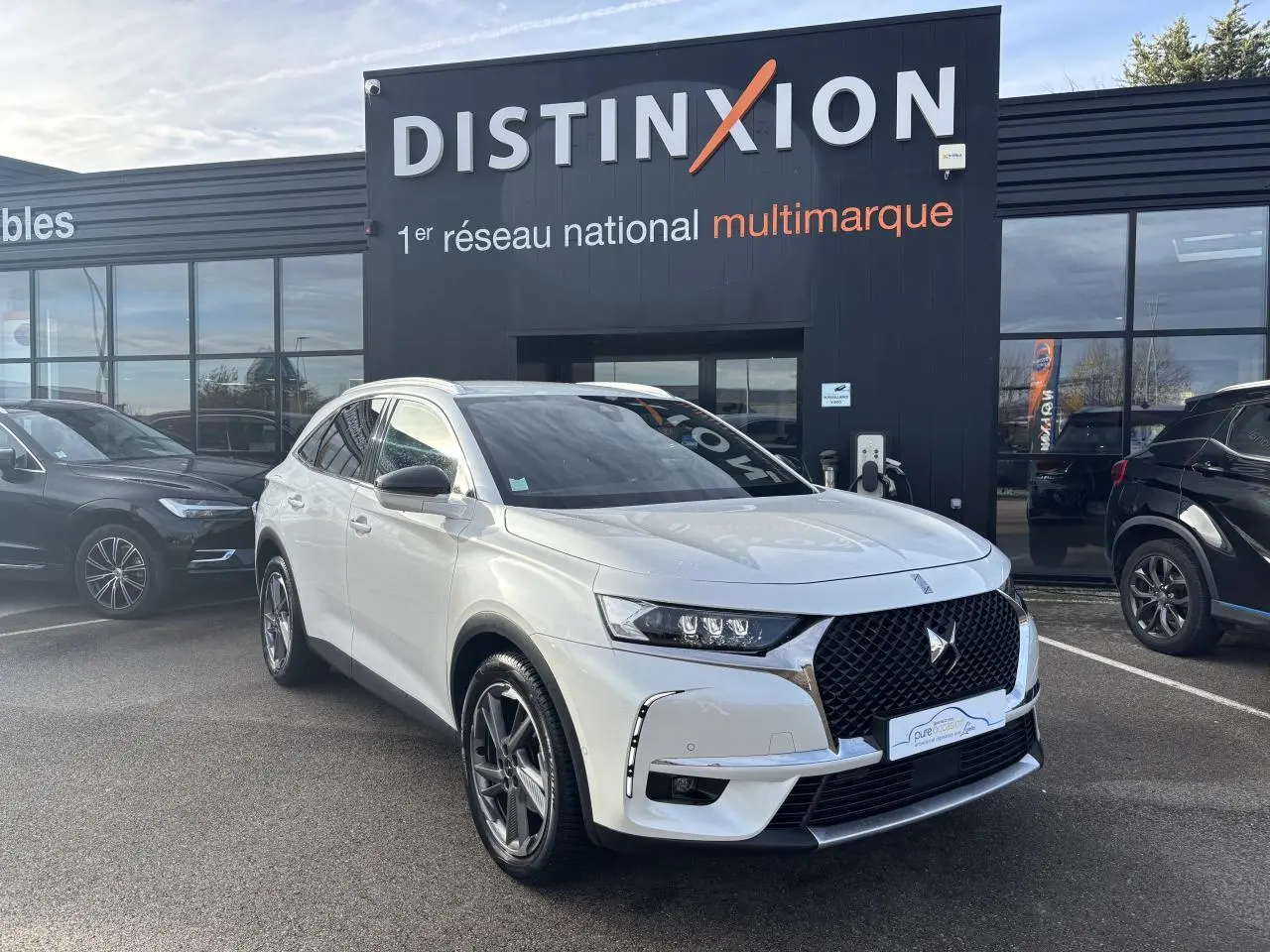 DS7 Crossback blanc en 3/4 avant droit avec calandre noire et jantes alliage, stationné devant un bâtiment Distinxion.