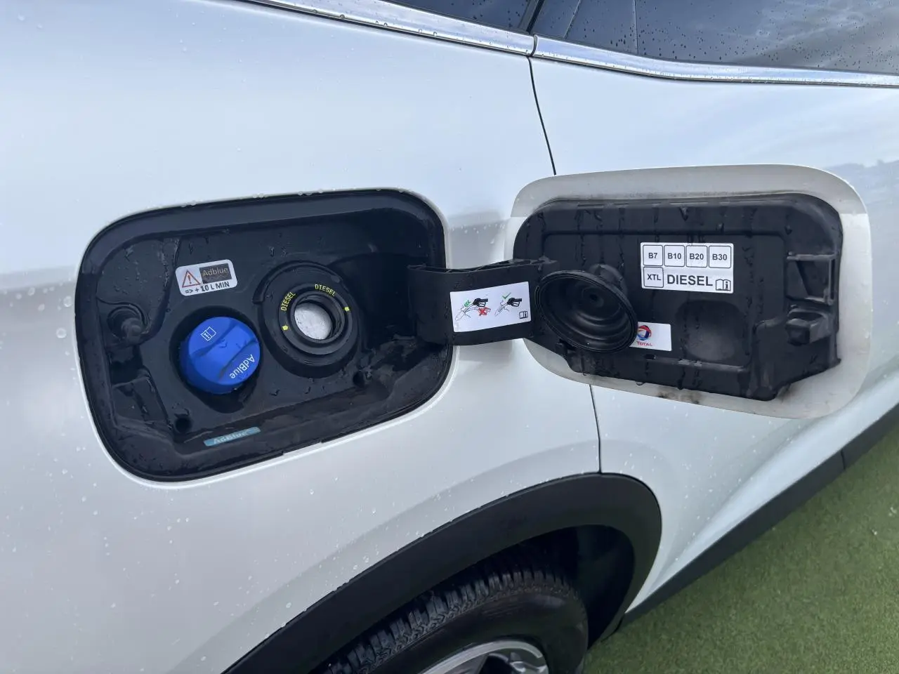 Trappe à carburant ouverte côté gauche du DS7 Crossback blanc nacré, montrant les bouchons diesel et AdBlue.