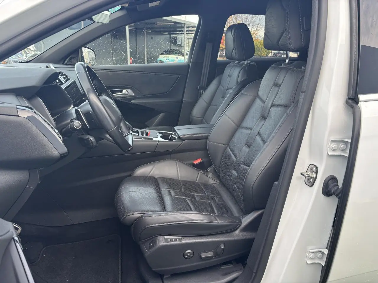 Vue intérieure côté conducteur du DS7 Crossback blanc avec sièges avant en cuir noir et tableau de bord moderne.