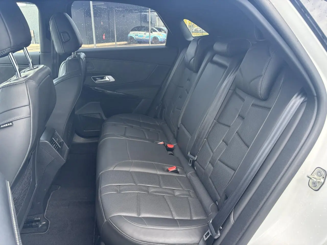 Vue latérale droite de l'habitacle arrière du DS7 Crossback blanc, avec sièges en cuir noir et ceintures visibles.
