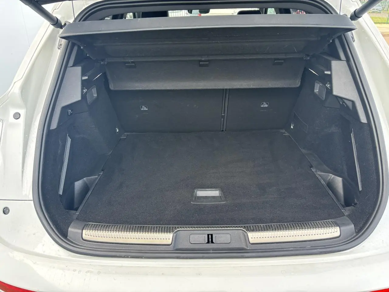 Coffre ouvert vu de l'arrière d'un DS7 Crossback blanc, avec tapis noir et cache-bagages déployé.