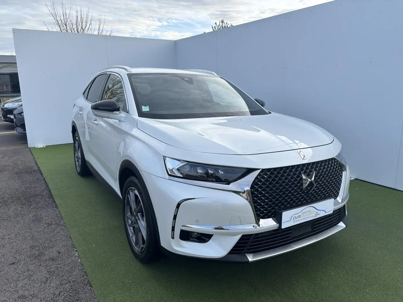 DS7 Crossback blanc en vue 3/4 avant gauche avec calandre DS Wings chromée et phares LED distinctifs.