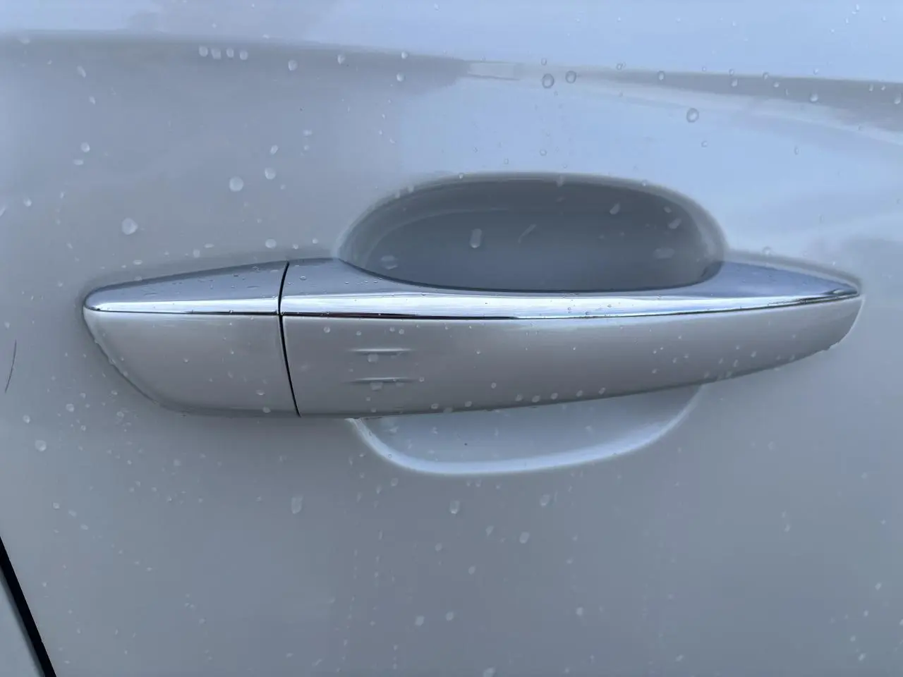 Poignée de porte chromée sur la portière blanche côté gauche du DS7 Crossback 2021, avec gouttes d'eau visibles.