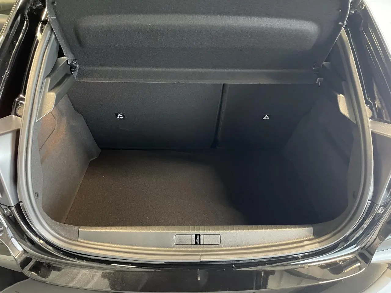 Coffre ouvert vu de l'arrière d'une Peugeot 208 noire, montrant un espace de rangement vide et propre.