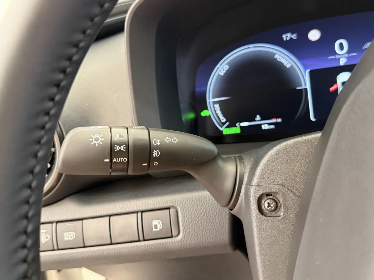 Gros plan sur la manette de phares et clignotants à gauche du volant dans le tableau de bord du Toyota C-HR blanc 2024.