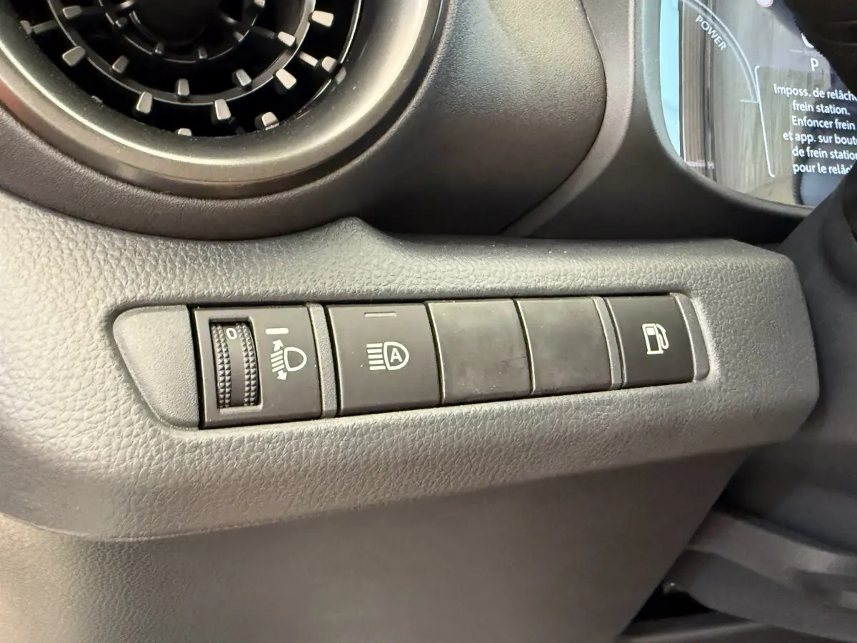 Gros plan sur les commandes de réglage des phares et ouverture du réservoir du Toyota C-HR 1.8 Hybride blanc, côté gauche.