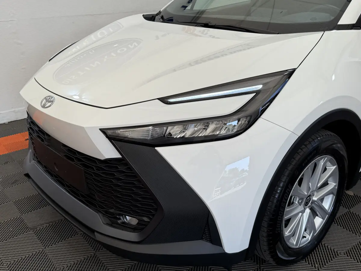 Vue 3/4 avant droit du Toyota C-HR 1.8 Hybride blanc, mettant en valeur ses phares LED et sa calandre noire texturée.