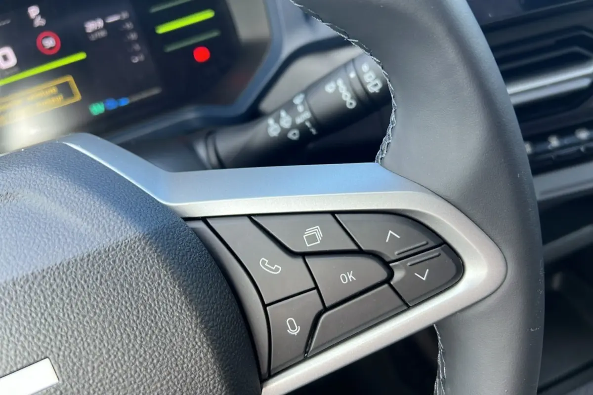 Gros plan sur les commandes au volant cuir du Dacia Bigster Hybrid 155 Expression Plus, avec écran digital en arrière-plan.