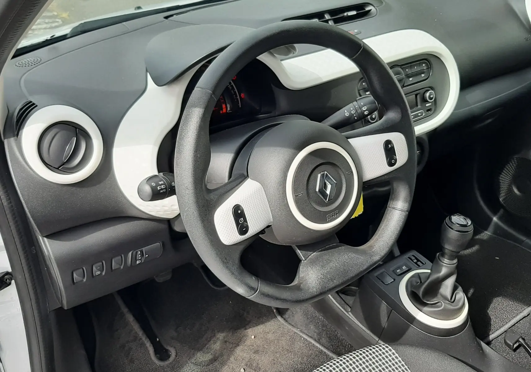 Vue intérieure côté conducteur de la Renault Twingo III blanc cristal, volant multifonction et levier de vitesse manuel visibles.
