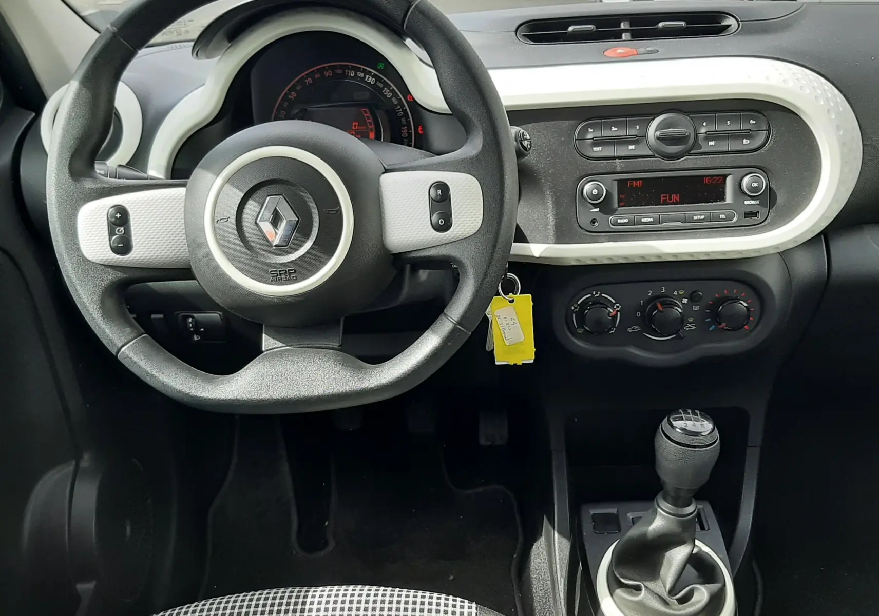 Vue intérieure du tableau de bord et volant de la Renault Twingo III blanche, avec levier de vitesse manuel et commandes centrales visibles.