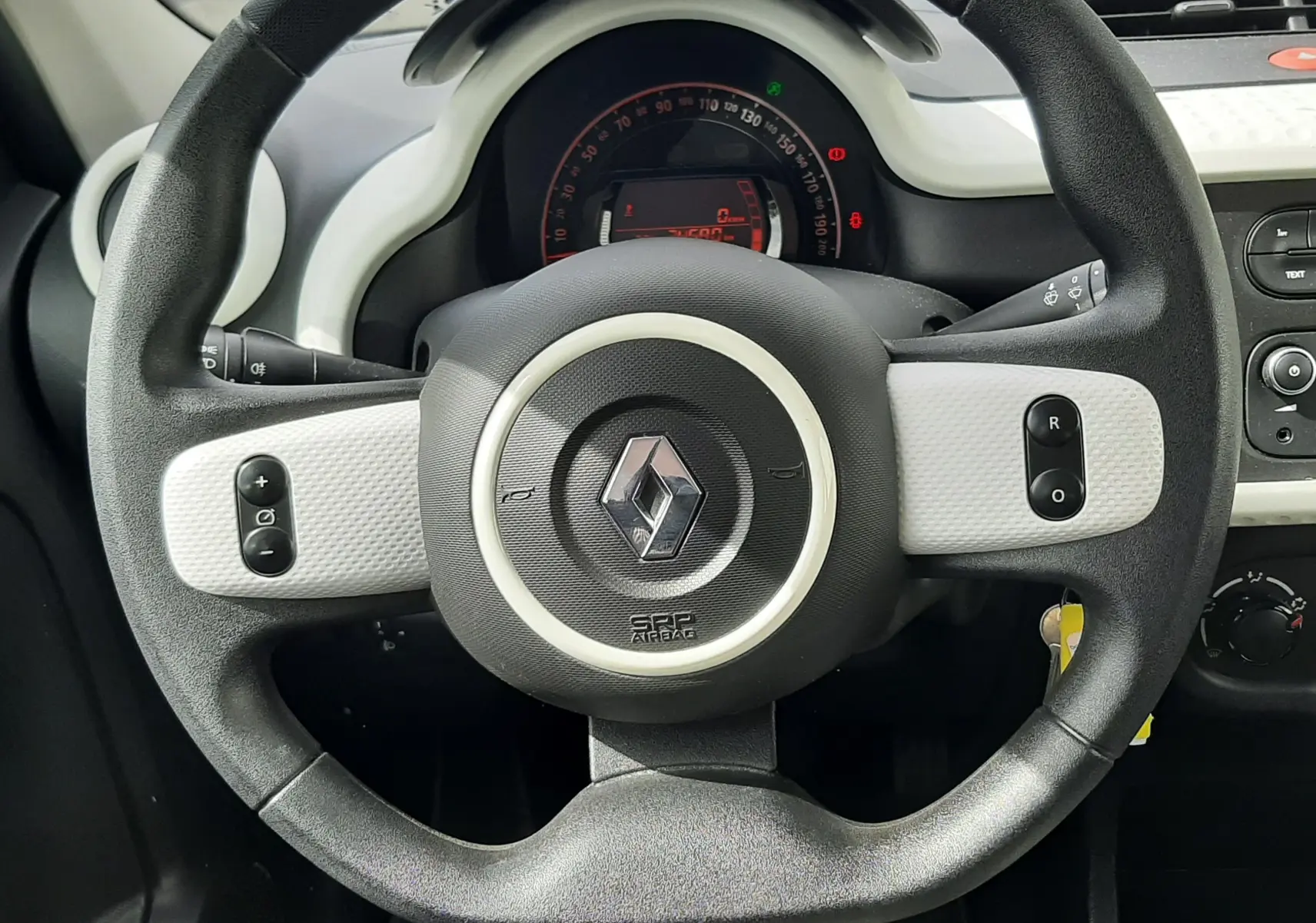 Vue rapprochée du volant noir et blanc de la Renault Twingo III 2021, avec tableau de bord numérique en arrière-plan.
