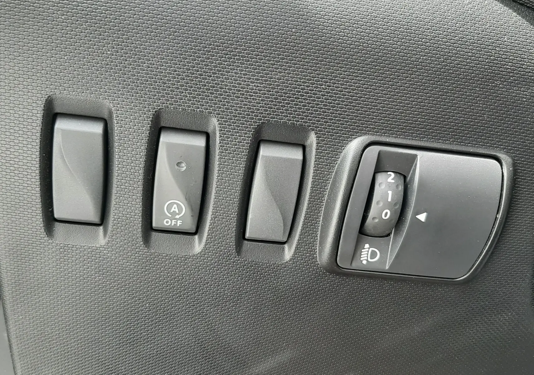 Panneau de commandes intérieures noires avec interrupteurs et molette de réglage des phares dans une Renault Twingo III blanc cristal.