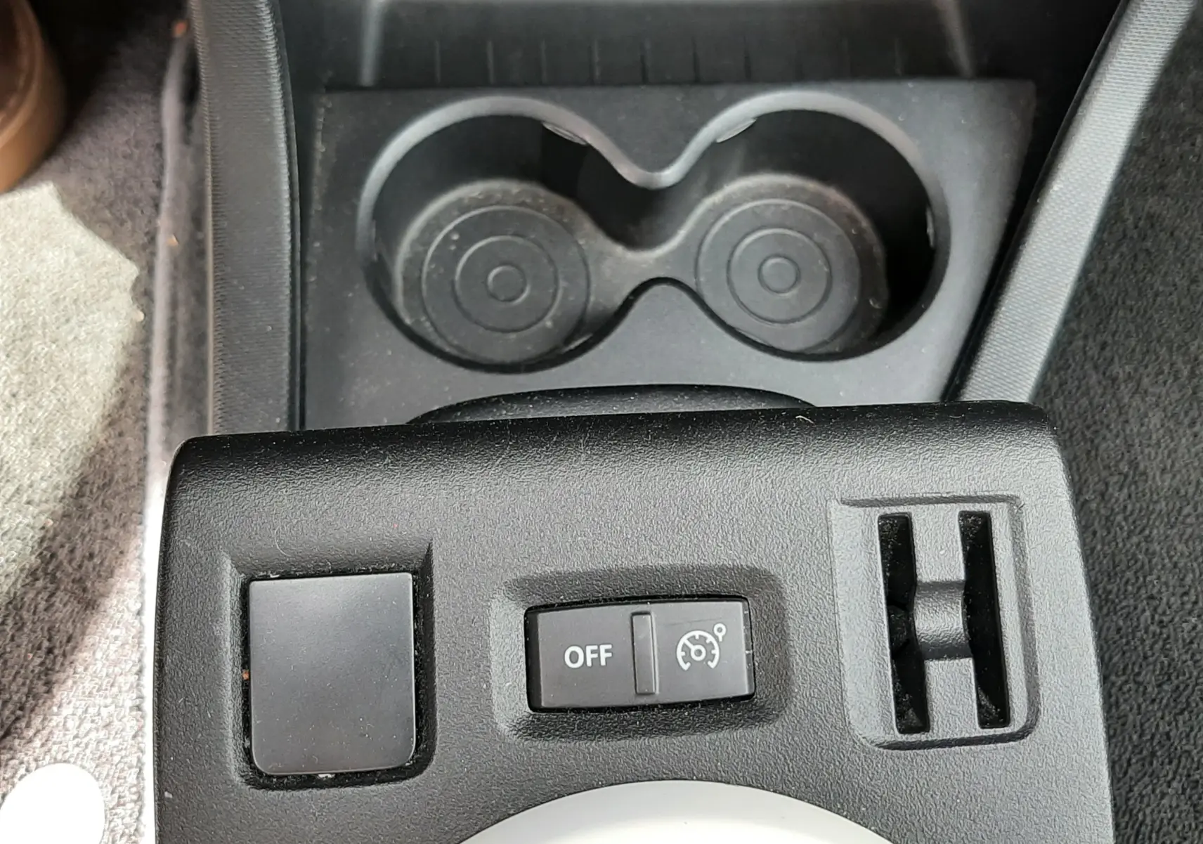 Vue rapprochée du tableau de commande noir avec bouton de régulateur de vitesse et porte-gobelets dans une Renault Twingo III blanc cristal.