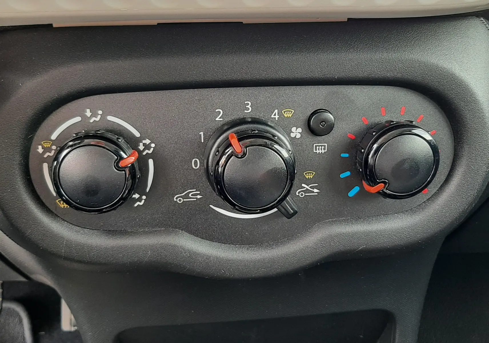 Vue rapprochée des commandes de climatisation noires sur tableau de bord gris d'une Renault Twingo III blanche.