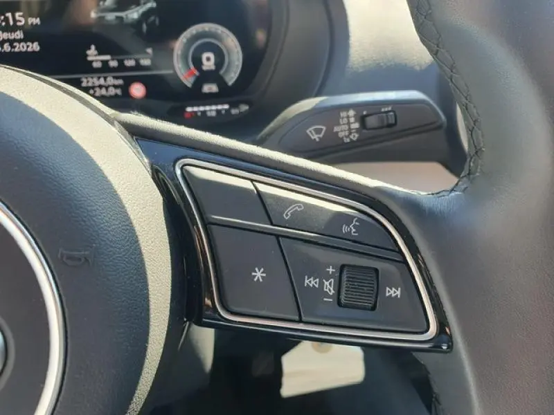 Gros plan sur les commandes du volant cuir multifonction de l'Audi Q2 gris Manhattan, avec tableau de bord numérique en arrière-plan.