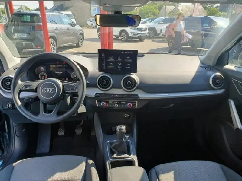 Vue intérieure avant de l'Audi Q2 30 TDI 116ch Design 2025, tableau de bord avec écran central et volant cuir multifonction.