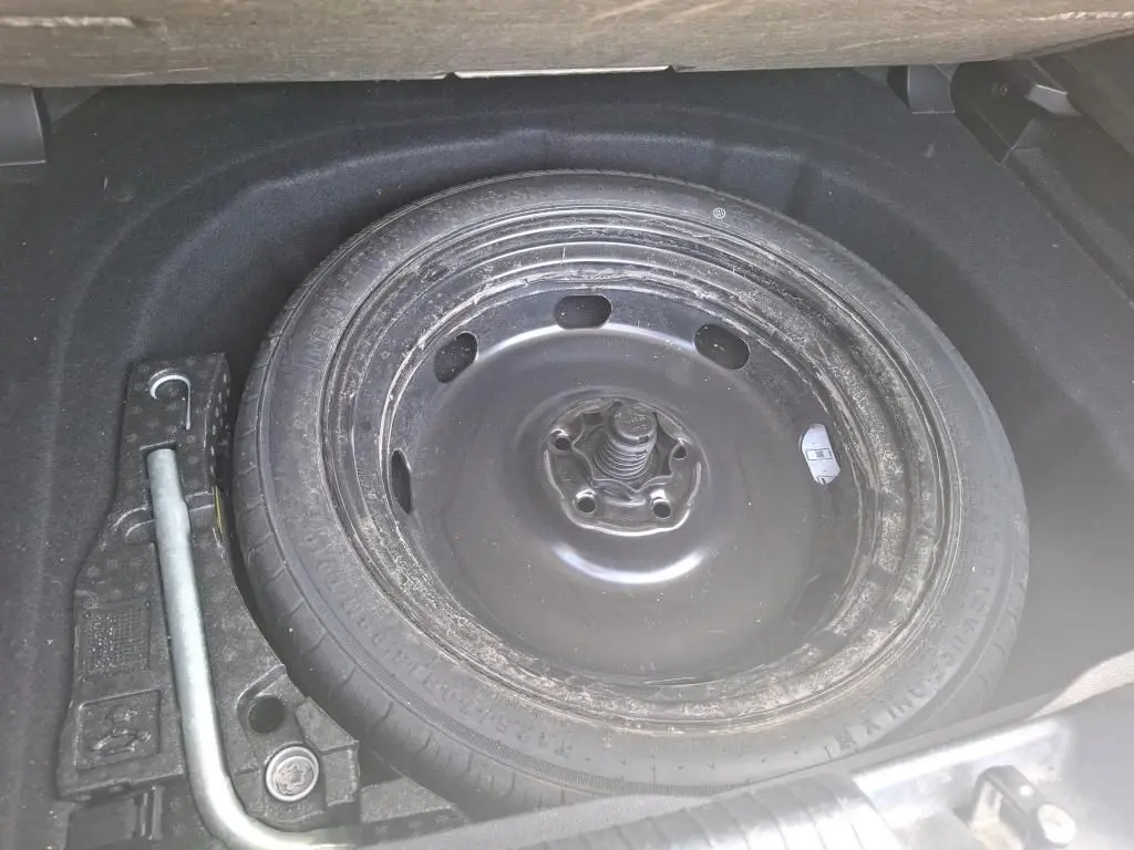 Gros plan sur la roue de secours noire et les outils dans le coffre d’une Volkswagen Golf gris clair 2023.