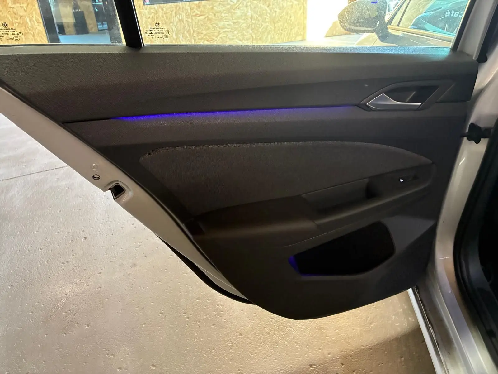 Vue intérieure de la porte arrière droite d'une Volkswagen Golf gris clair 2023 avec éclairage d'ambiance bleu.