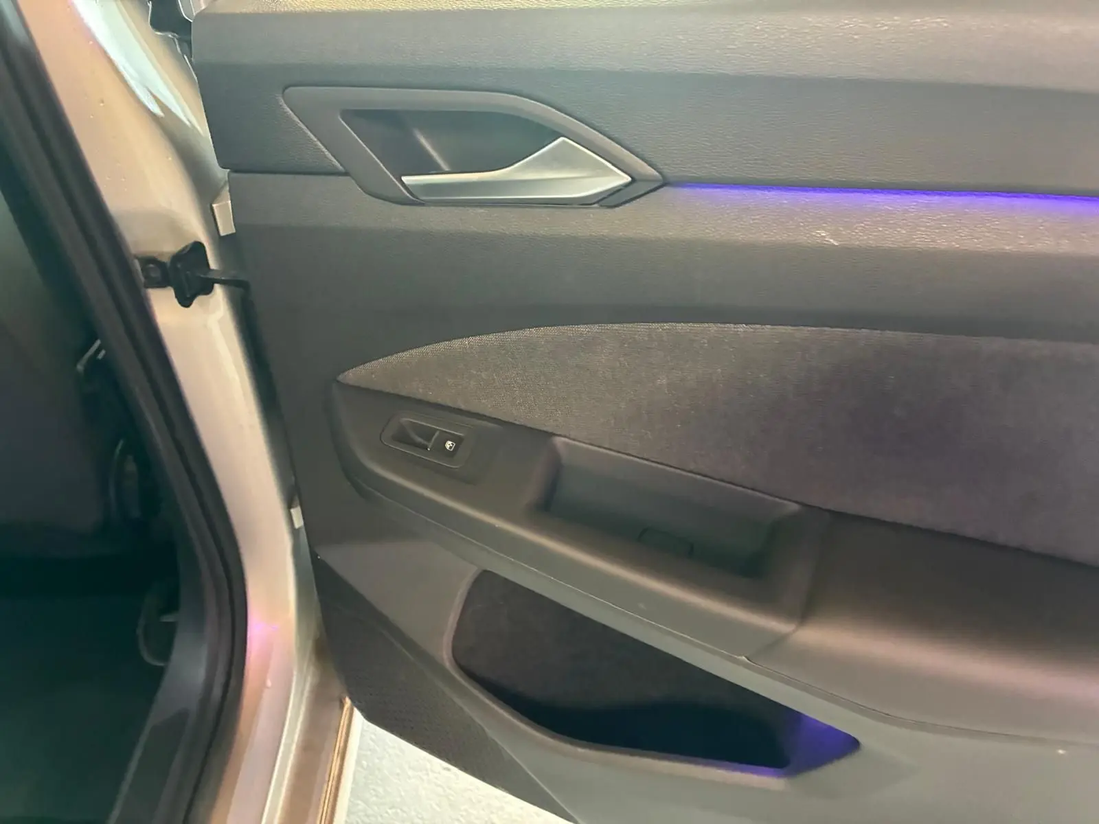 Gros plan sur la porte intérieure côté gauche d'une Volkswagen Golf gris clair avec éclairage d'ambiance violet.