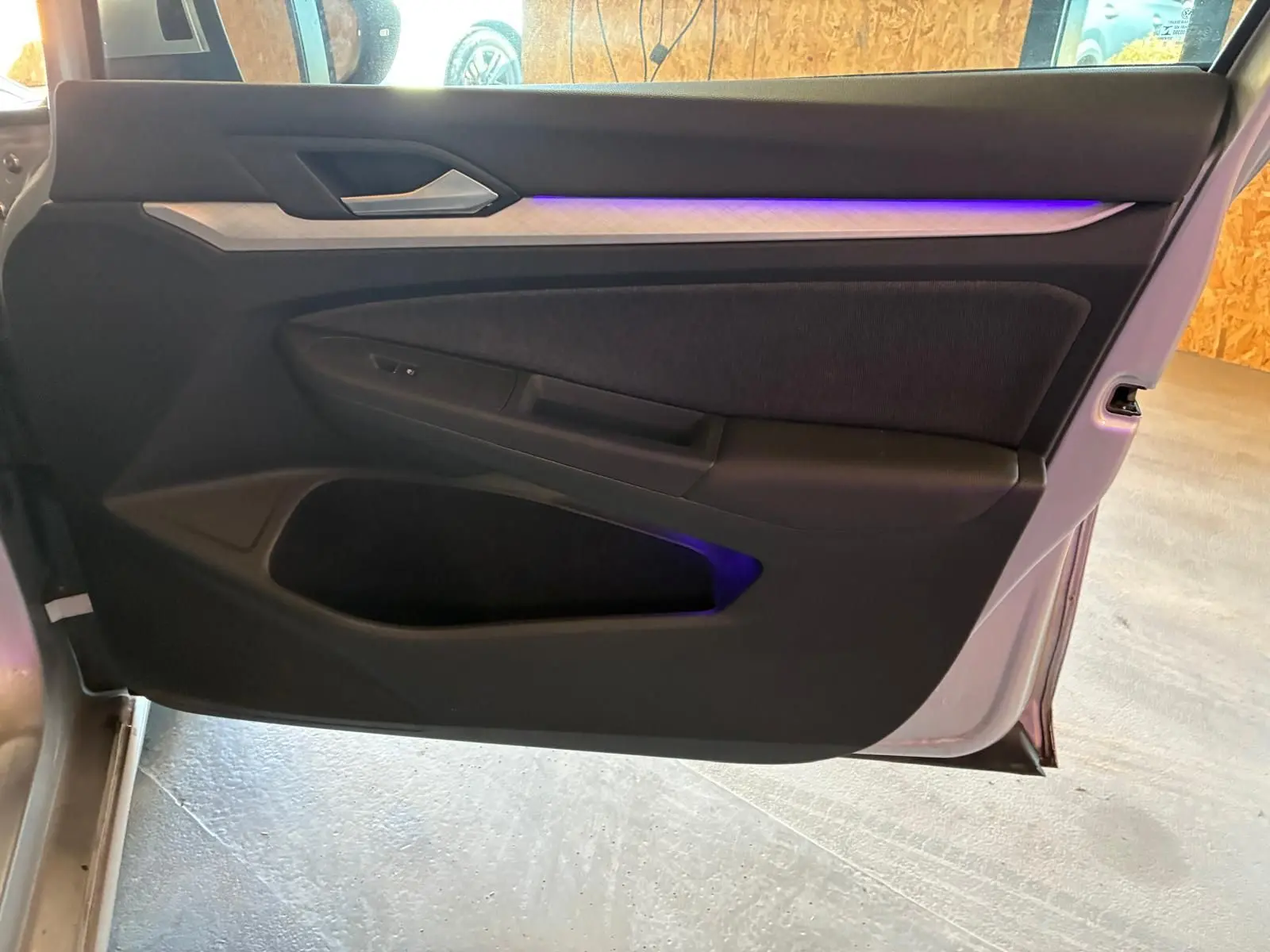 Vue intérieure de la porte avant gauche d'une Volkswagen Golf gris clair 2023 avec éclairage d'ambiance violet.