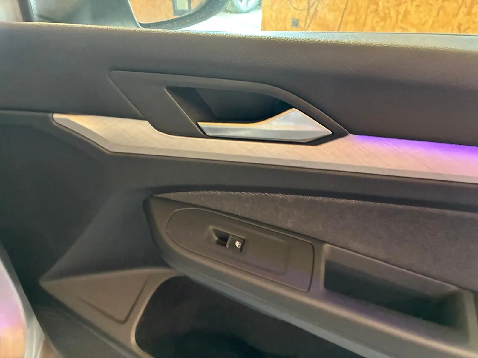 Détail de la porte côté gauche de la Volkswagen Golf 2023, avec insert décoratif clair et éclairage d'ambiance violet.