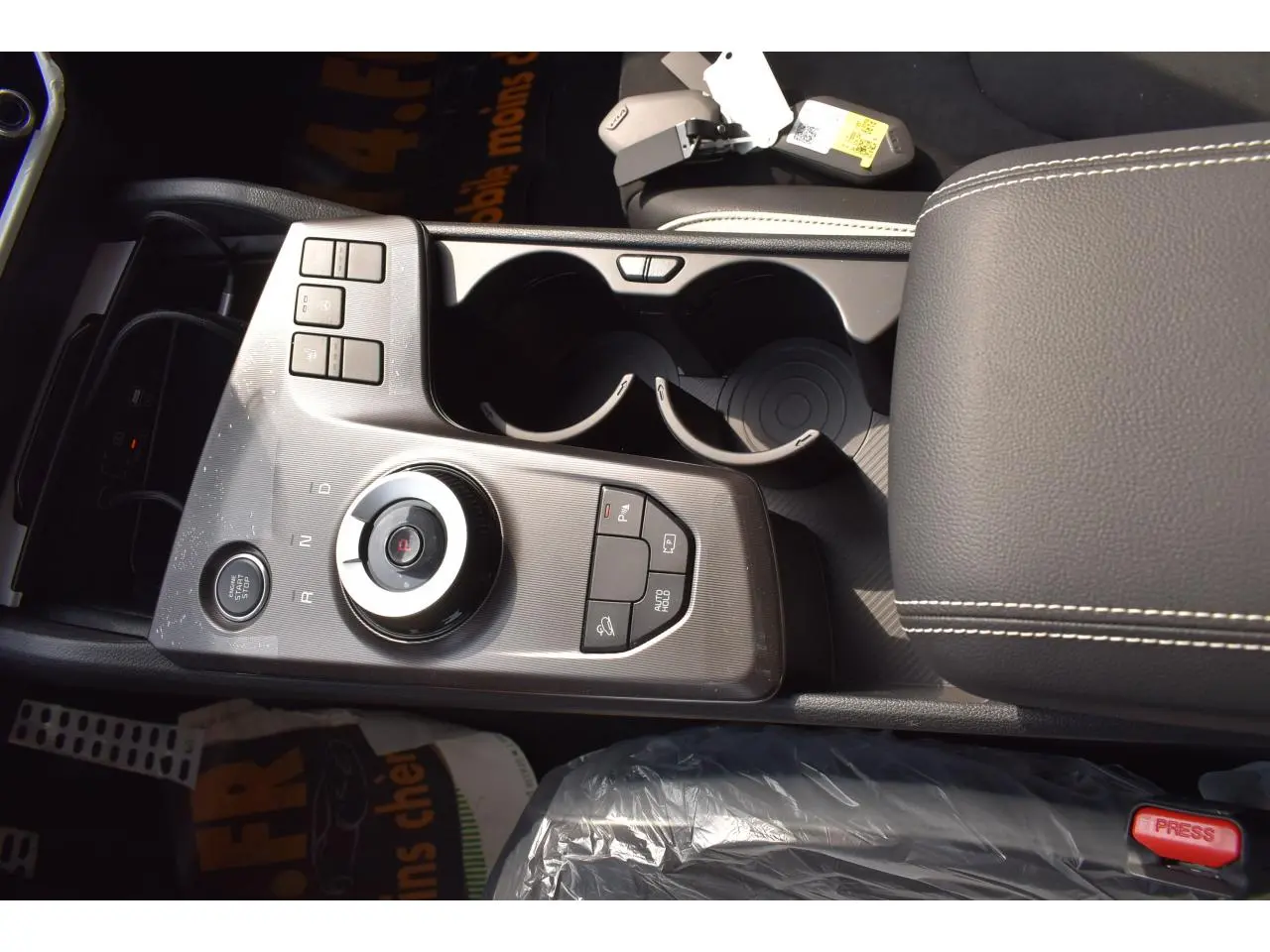 Vue rapprochée de la console centrale grise du Kia Sportage hybride 2026 avec sélecteur rotatif et accoudoir cuir noir.