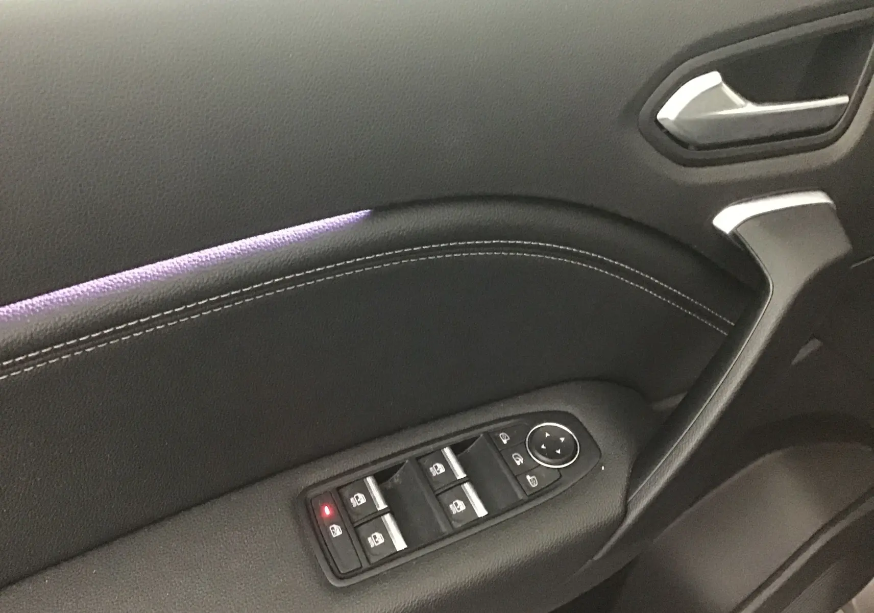Gros plan sur la porte côté gauche du Renault Captur 2024 gris Cassiopée/Noir avec commandes électriques et éclairage d'ambiance violet.