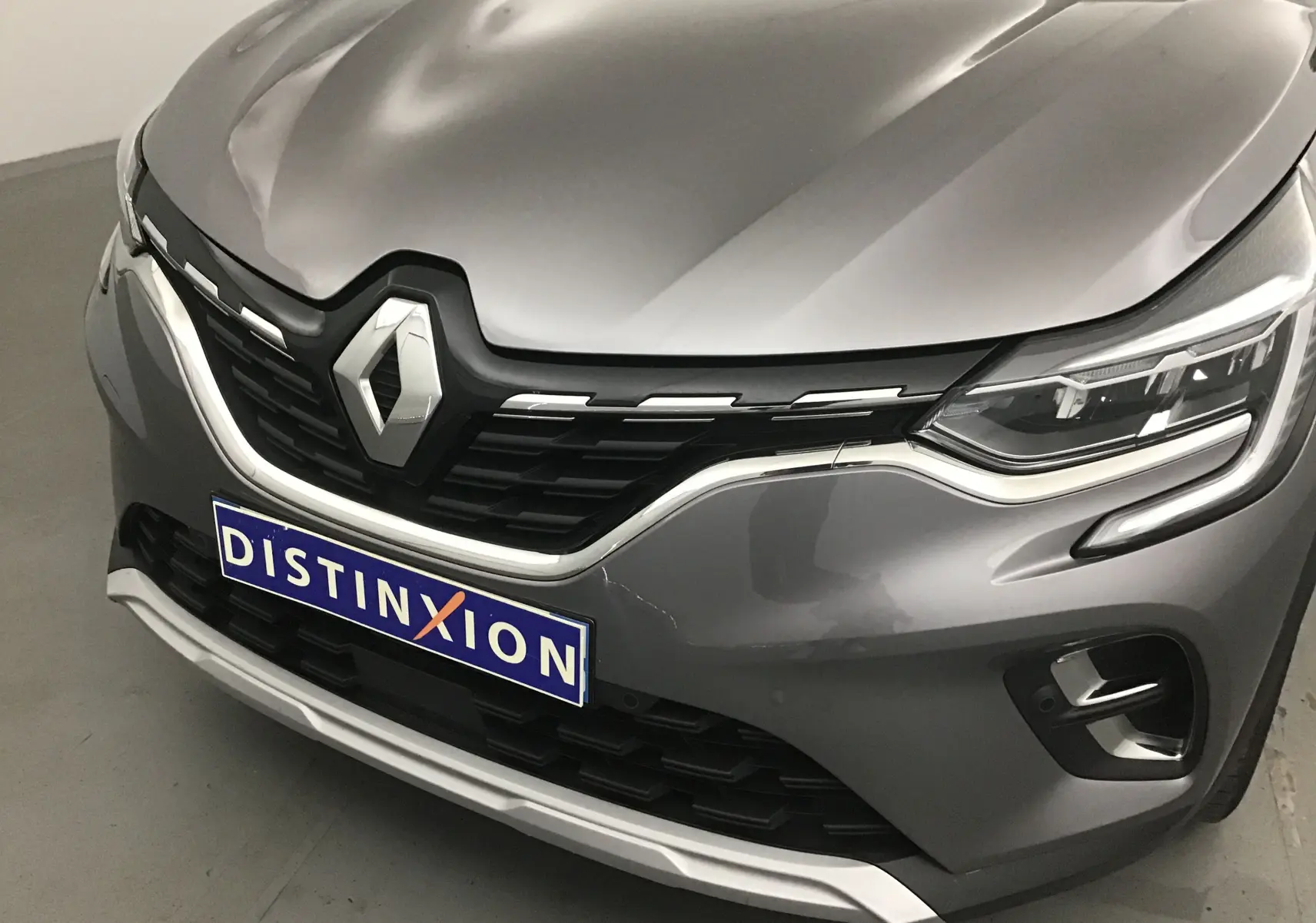 Vue avant rapprochée du Renault Captur gris Cassiopée avec calandre noire et logo chromé bien visible.