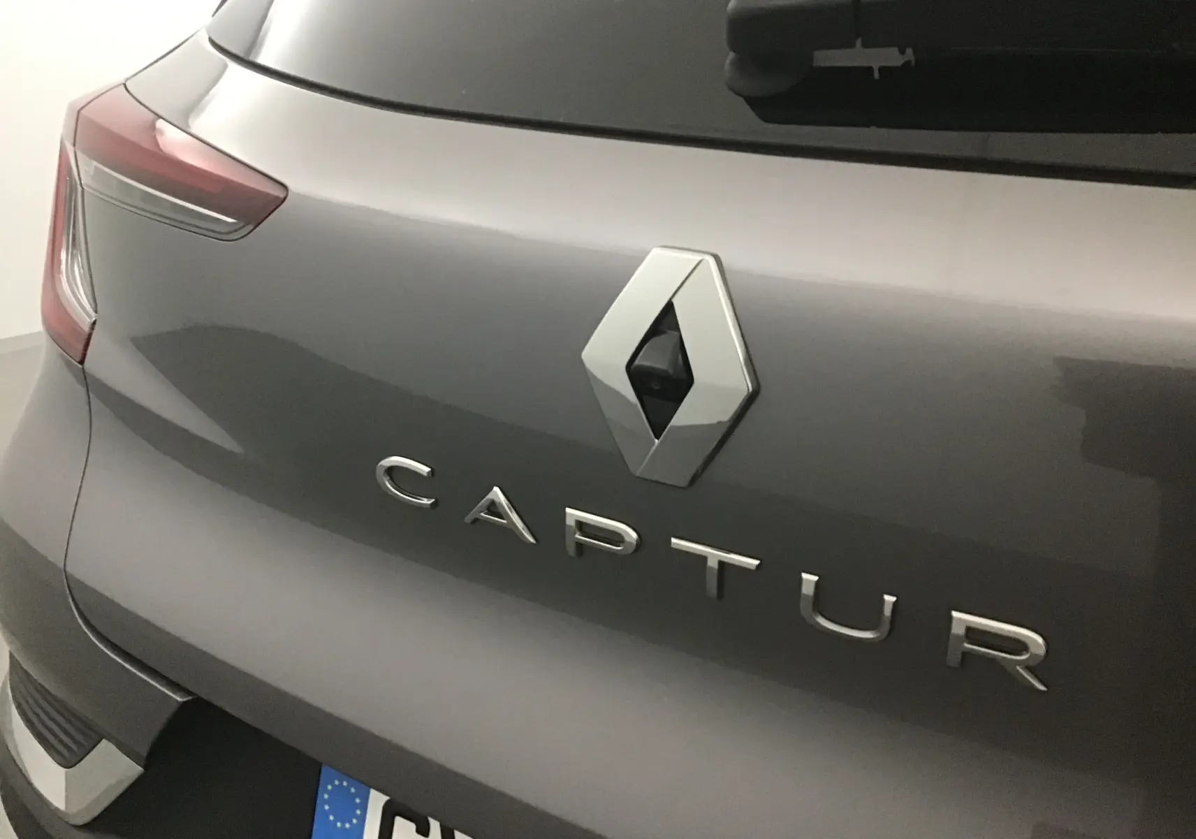 Gros plan sur l'arrière gris cassiopée du Renault Captur 2024, mettant en valeur le logo et la caméra de recul intégrée.