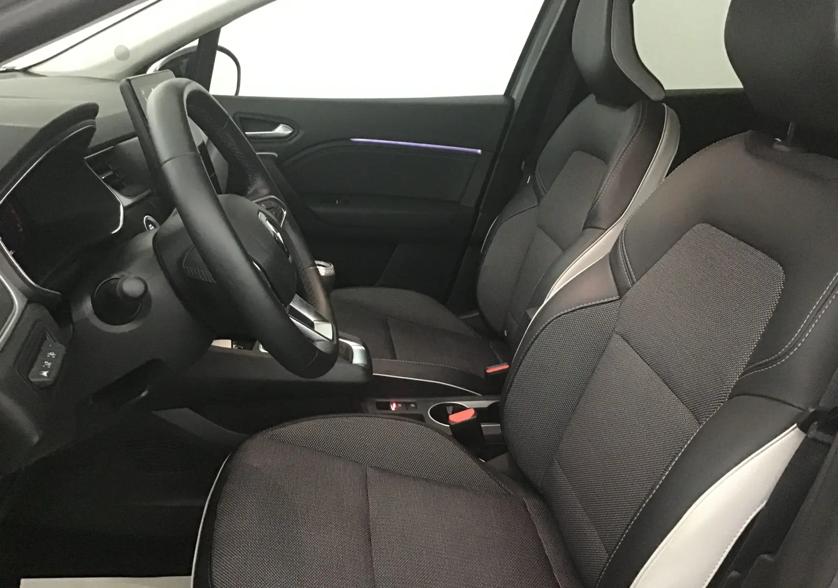 Vue intérieure côté conducteur du Renault Captur 2024 avec sièges gris et noir et éclairage d'ambiance violet sur la portière.