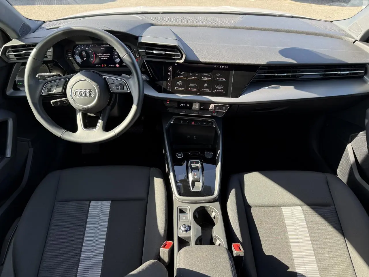 Vue intérieure avant de l'Audi A3 Sportback 2024 avec tableau de bord noir et volant cuir multifonctions.