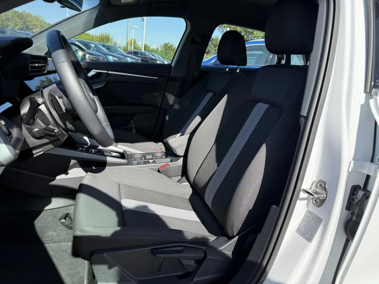 Intérieur côté conducteur de l'Audi A3 Sportback blanc Arkona 2024 avec sièges tissu noir et gris et volant cuir multifonctions.