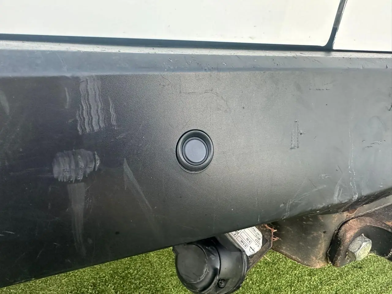 Gros plan sur le pare-chocs arrière noir du Ford Transit Connect blanc, avec prise de remorquage visible en bas à droite.