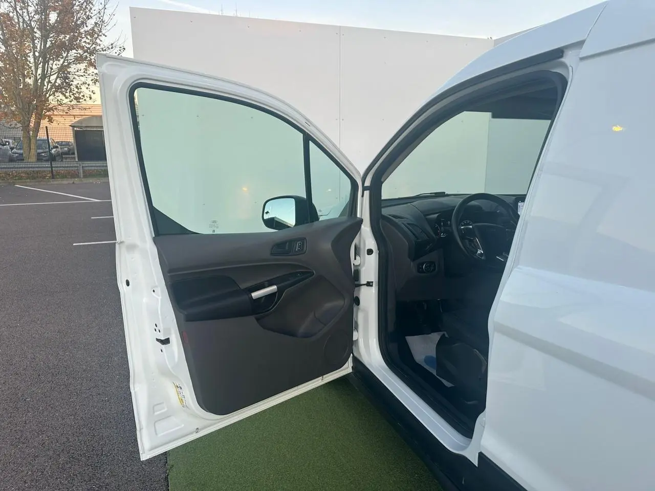 Portière avant gauche ouverte d'un Ford Transit Connect blanc, montrant l'intérieur noir et le tableau de bord côté conducteur.