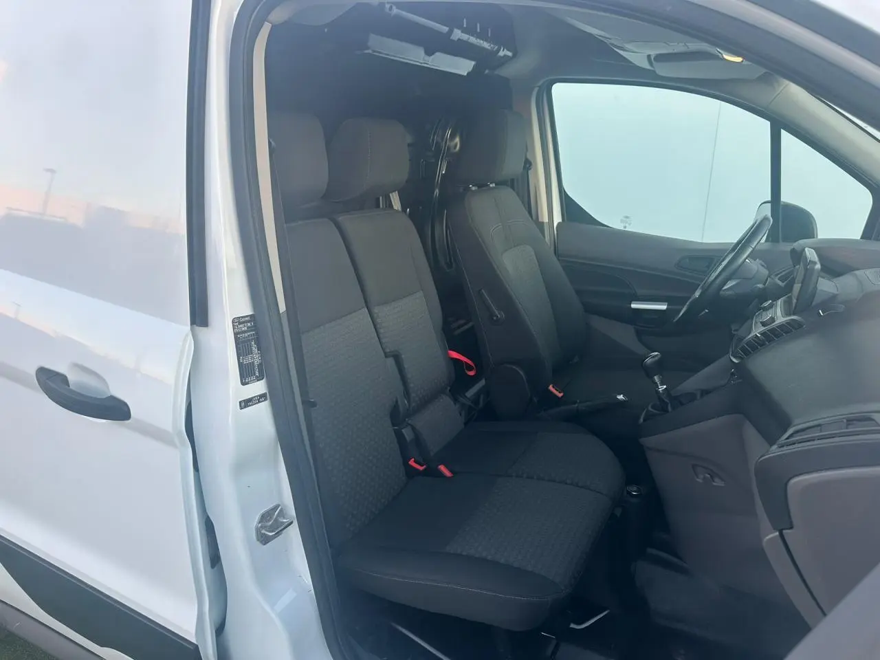 Vue intérieure côté conducteur du Ford Transit Connect blanc de 2019, montrant les sièges avant et le tableau de bord.