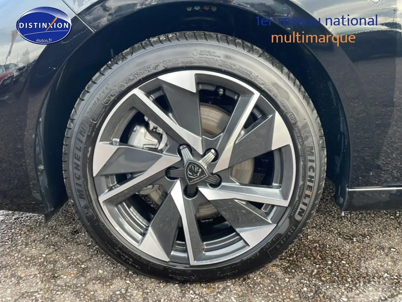 Gros plan sur la roue avant droite noire d'une Peugeot 308 1.2 hybrid 145 allure e-dcs6 avec jante alu bicolore.