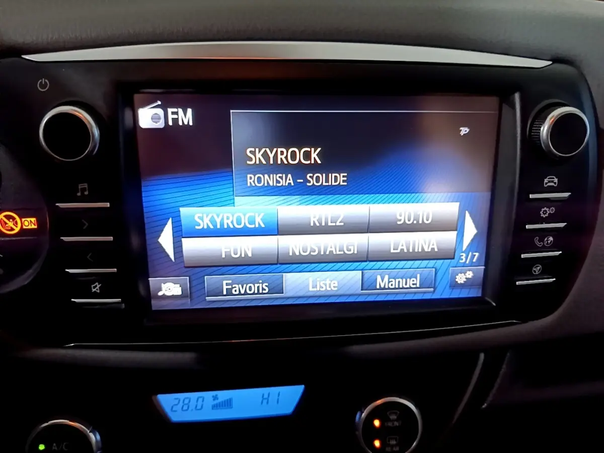 Écran tactile central de la Toyota Yaris blanche 2020 affichant la radio FM sur Skyrock, avec commandes autour.
